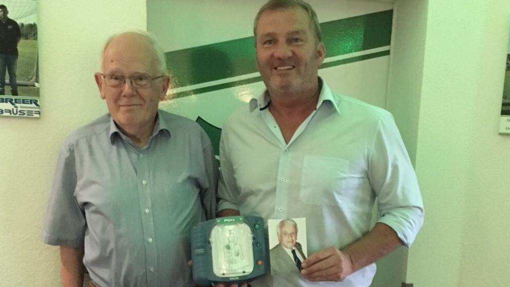 Ulrich Springob (l.) und Michael Berghaus, der ein Foto des verstorbenen "Seppel" Springob in der Hand hält, präsentieren stolz den neuen Defibrillator. von privat