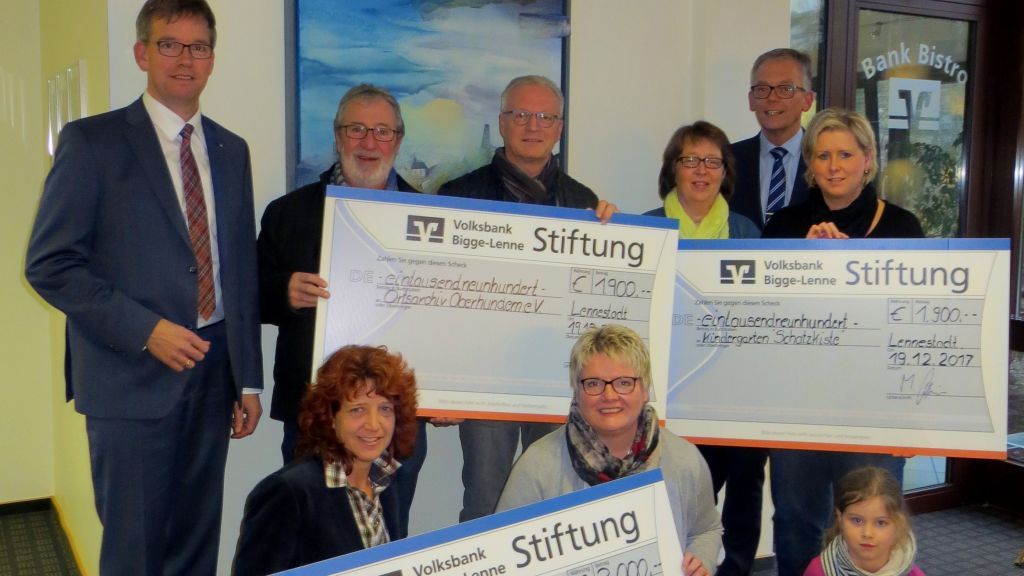 Vorstandsmitglied Michael Griese (links) und Regionalmarktleiter Bernd Kramer (hinten rechts) belohnen das ehrenamtliche Engagement von Beatrice Hartmann und Ilona Halbe (Caritas), Wendelin Kebbe und Thomas Richter (Ortsarchiv Oberhundem), Stefanie Alf und Katja Baumann mit Tochter Mia (Kindergarten Schatzkiste). von Volksbank Bigge-Lenne