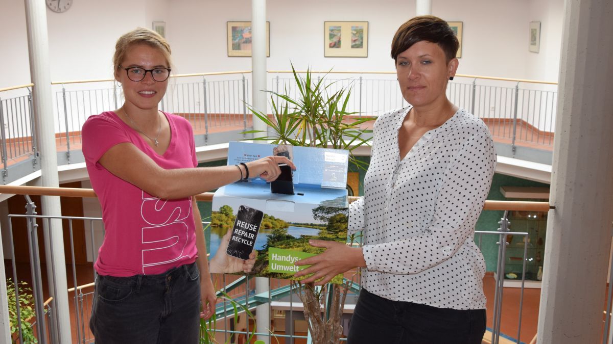 Sophia Werthenbach und Katrin Schröder (von links) präsentieren die neue Sammelbox für alte Handys im Wendener Rathaus. von Gemeinde Wenden