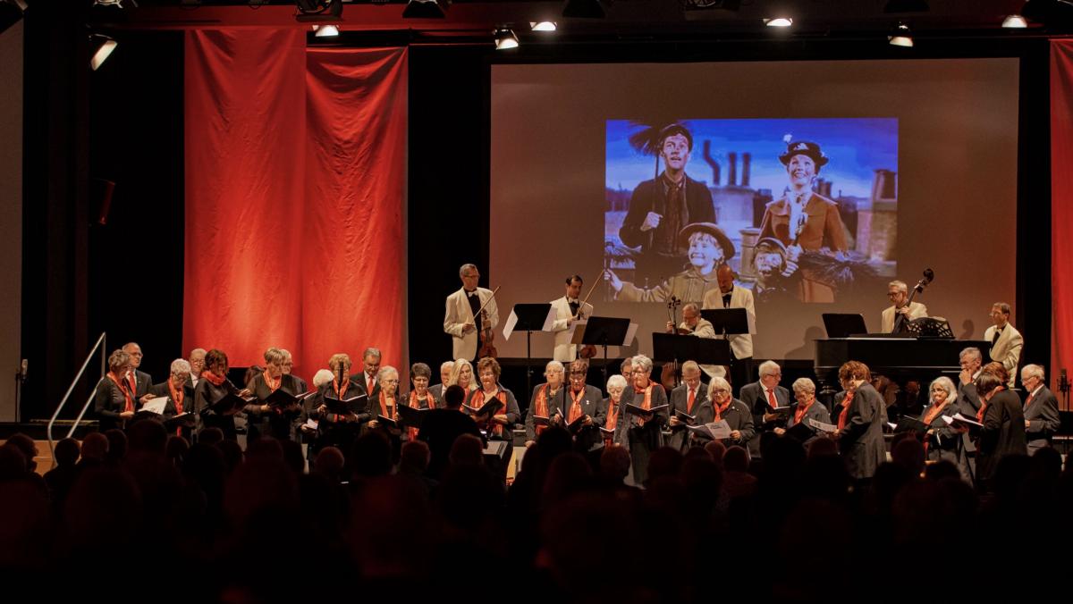 Der Chor Cäcilia Attendorn mit dem Ensemble Salonlöwen – Im Hintergrund eine Szene aus dem Mary Poppins Medley „Chim Chim Cherie“. von Tramo Medienagentur
