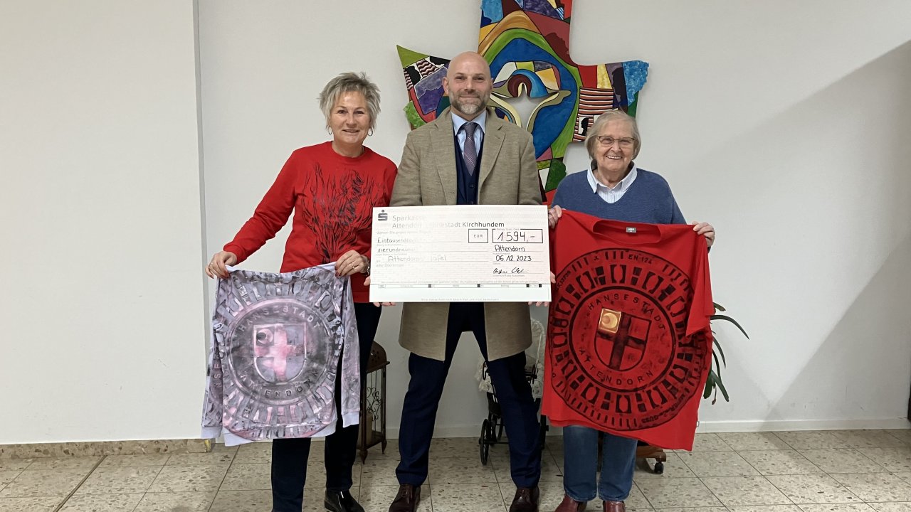 Qualitätsmanager und Auditor Christian Waldau aus Plettenberg überreichte einen symbolischen Scheck in Höhe von 1595 Euro an die Attendorner Tafel. Die Gäste von Frühlingsmarkt und HanseNacht hatten gegen eine Spende T-Shirts mit Gullydeckel-Motiv erworben. Die Spende gab der Initiator der sozialen Kreativ-Aktion jetzt weiter - mit einer außergewöhnlichen Anregung. Spendenübergabe mit Beate Waldau, Christian Waldau und Sylvelin Karsunky als Vertreterin der Attendorner Tafel (v.l.n.r.). von privat