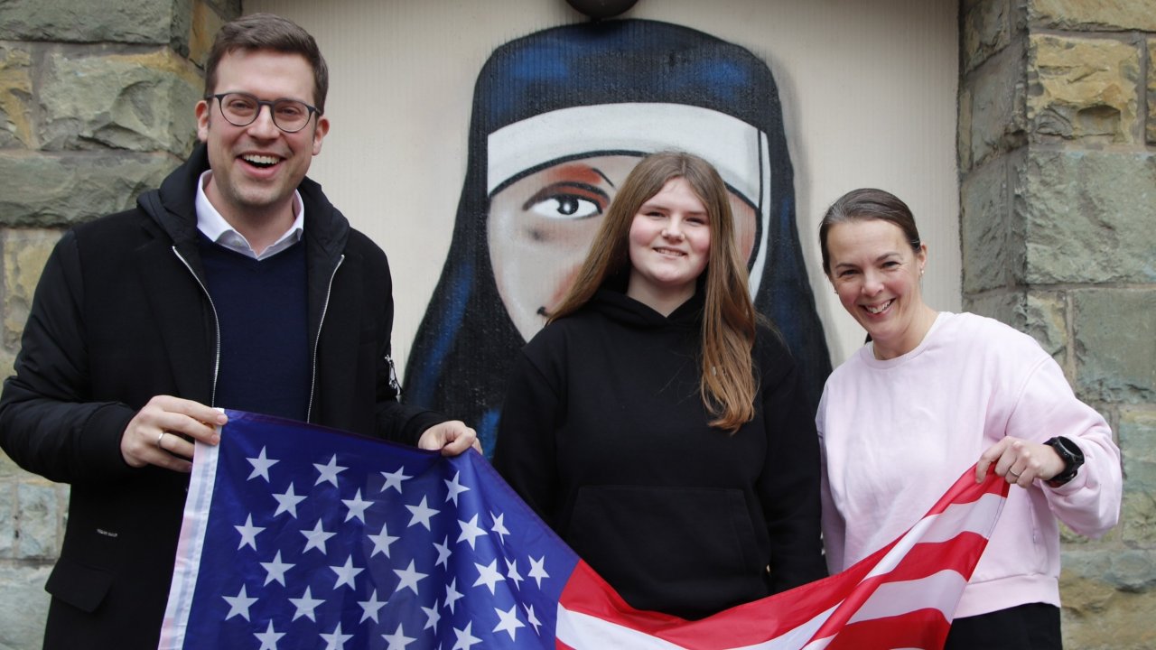 Mit der US-Fahne in der Hand und einem Lächeln im Gesicht: Jana Schäfer nimmt ihr PPP-Stipendium entgegen – flankiert von Bundestagsabgeordnetem Florian Müller (CDU) und ihrer Klassenlehrerin Anke Ackerschott von privat