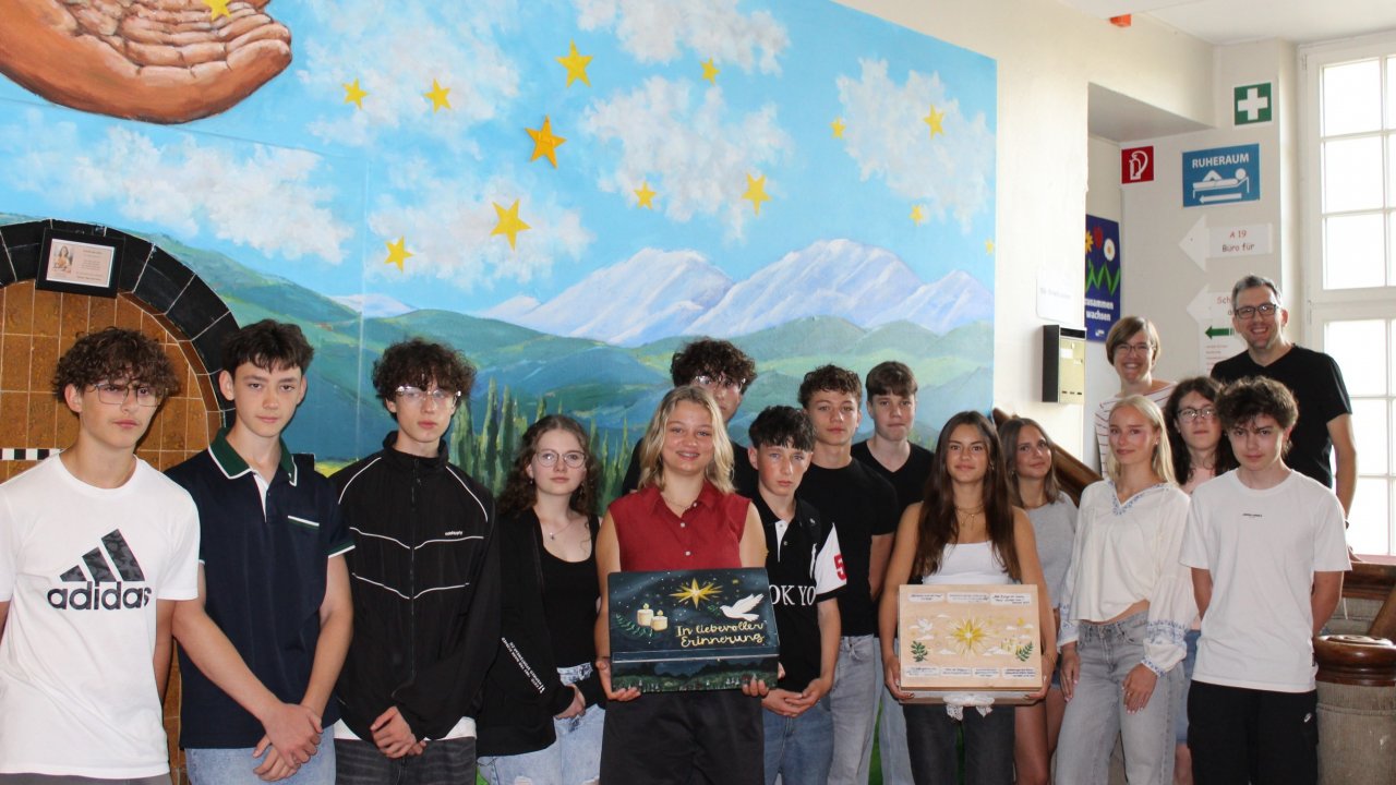 Der Religionskurs der neunten Klassen präsentiert die fertigen Trauer- und Erinnerungskisten vor der Gedenkwand im Altbau des Städtischen Gymnasiums. Das Projekt haben Religionslehrerin Henrike Neumann und Schulsozialarbeiter Frank Böhm begleitet. von privat