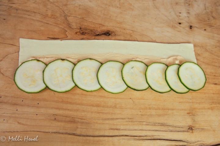 Bestreicht die Blätterteigstreifen mit pikantem Frischkäse, belegt sie hälftig mit Zucchinischeiben, die ihr mit Salz und Pfeffer würzt...