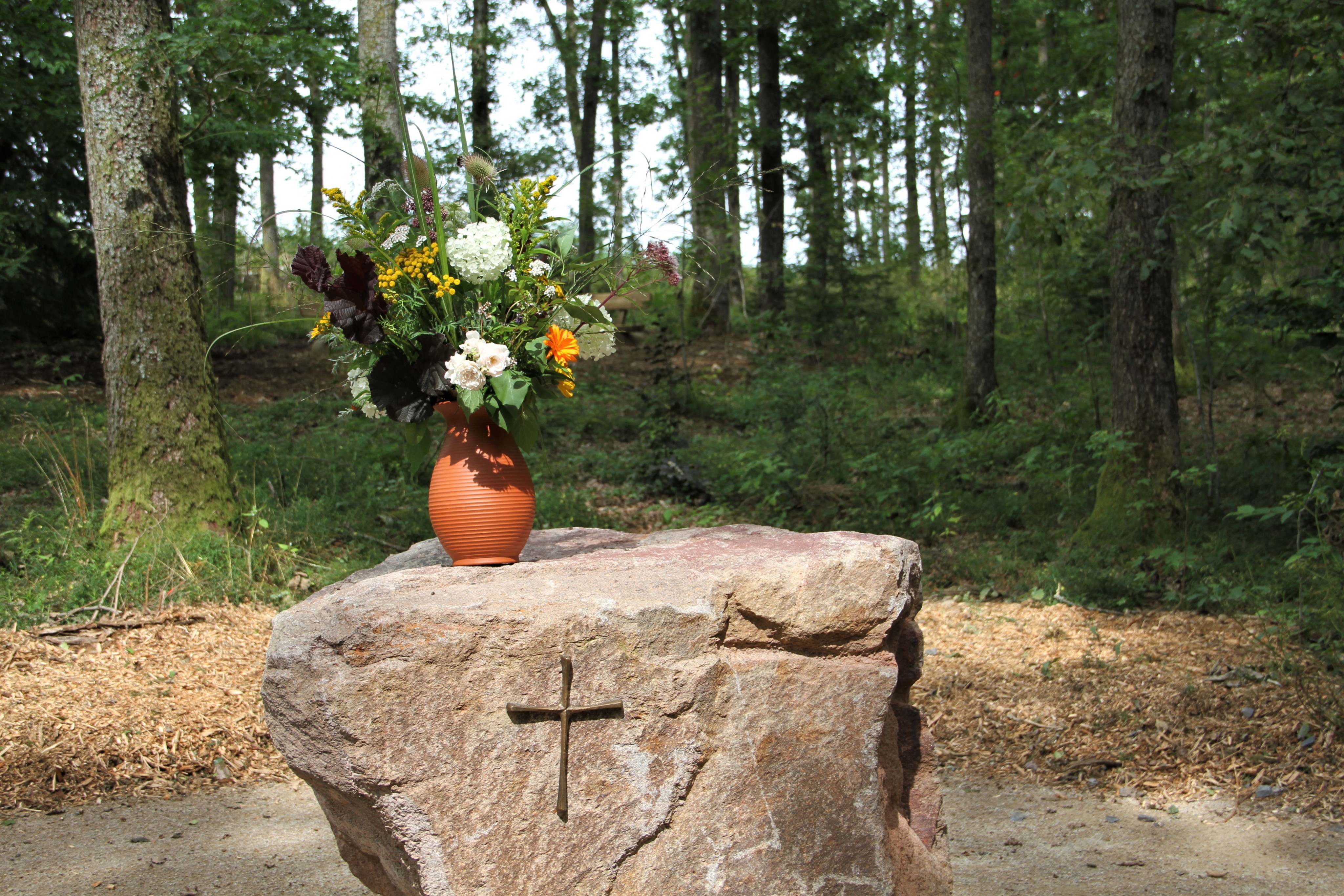 Ein großer Fels, schlicht geschmückt mit einem Kreuz, markiert das Zentrum des Waldfriedhofs. An den Platz grenzen die verschiedenen Bestattungsbereiche, Ruhebänke laden zum Verweilen ein. von Kerstin Sauer